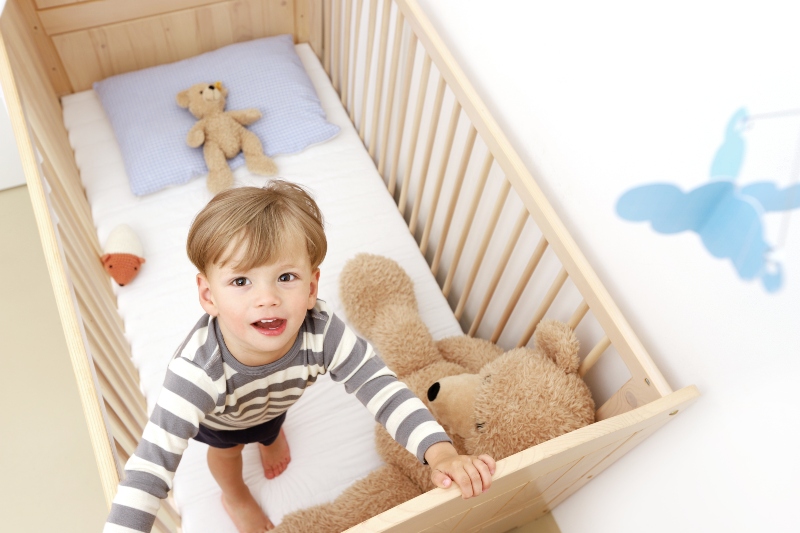 Ein zweijaehriger Junge steht in seinem Kinderbett